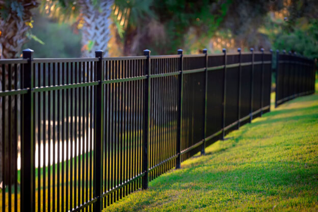 A black aluminum fence installed on a stretch of mowed grass with trees in the background.