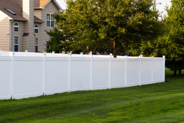 A white vinyl fence on a green lawn in a neighborhood.